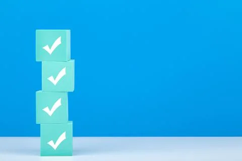 Checkmarks on four light blue toy blocks on white table against blue background Stock Photos