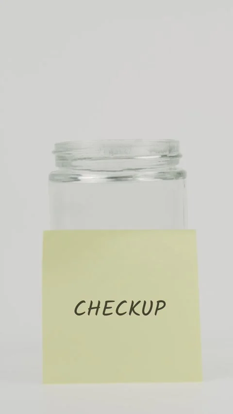 Checkup text or word on yellow sticky note attached to glass jar with hand Stock Footage 311690731