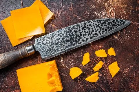 Cheddar Cheese sliced on a kitchen table with knife. dark background. Top view Stock Photos