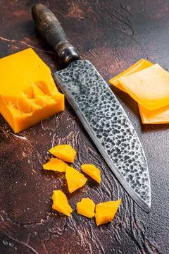 Cheddar Cheese sliced on a kitchen table with knife. dark background. Top view Stock Photos