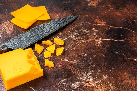 Cheddar Cheese sliced on a kitchen table with knife. dark background. Top view Stock Photos