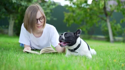 Cheeful student is reading book sitting in the park then patting adorable puppy  Vídeos de archivo 137033417
