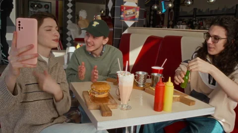 Cheeky Student Adding Chili Sauce to Friends Burger while Eating at Diner Stock Footage 335760112