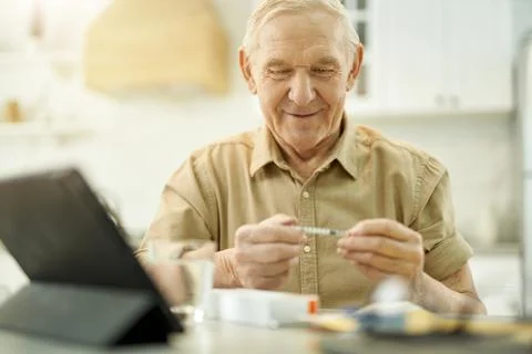 Cheered-up elderly man having a close look at syringe Stock Photos