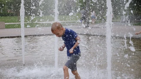 A cheerful active boy plays with a jet of water in a fountain in a city park. Stock Footage 296270483