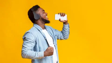 Cheerful african american man singing into smartphone like microphone Stock Photos
