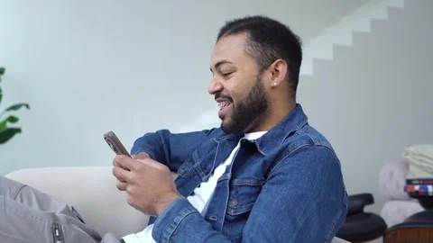 Cheerful african american man using smartphone and smiling at home Stock Footage 293828007