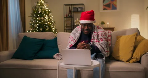 A cheerful African-looking guy sits on sofa in the living room and has video 動画素材 211217161
