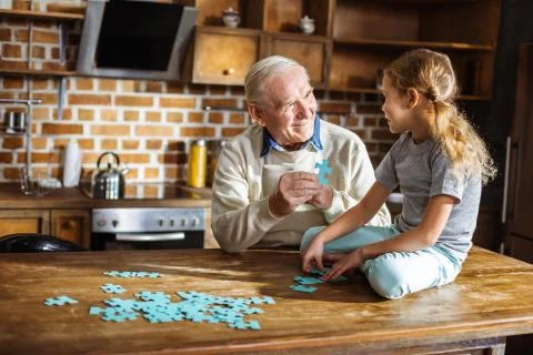Cheerful aged man assembling pazzles with his granddaughter Stock Photos