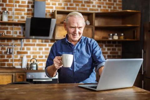 Cheerful aged man using his laptop in the kitchen Stock Photos