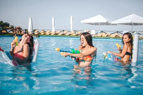 Cheerful and funny models playing in swimming pool. They hold water guns in h Foto stock