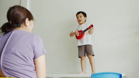 Cheerful Asian boy smiling while playing a red ukulele Stock Footage 292854123