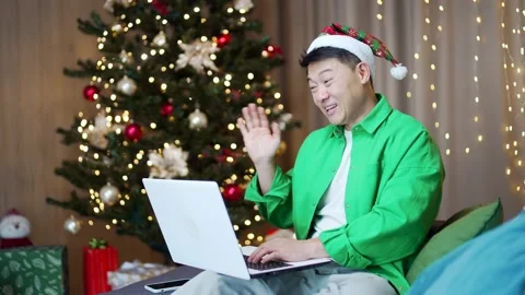 Cheerful asian man in a Santa hat is talking online on video call remotely. Happ Stock Footage 219916586