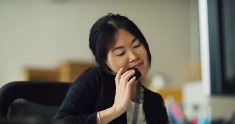 Cheerful Asian secretary answers phone in office during the daytime. Medium to c Stock Footage 199459624