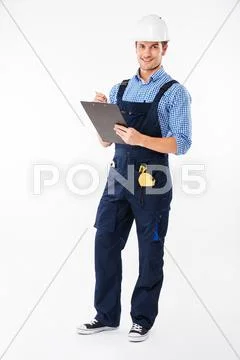 Cheerful attractive young builder standing and writing on clipboard Stock Photos