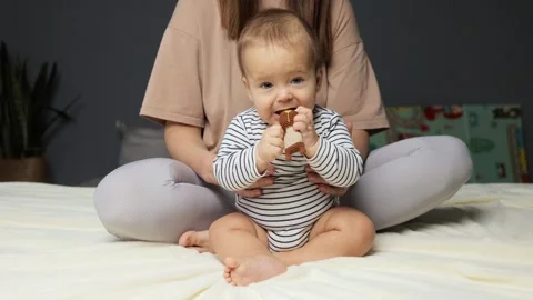 A cheerful baby sits on a bed, captivated by a soft toy in hand, while a Vídeo Stock 295675419