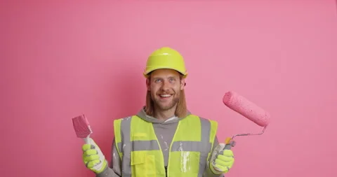 Cheerful bearded man paints interior wall of dwelling holds painting roller and Stock Footage 156225925
