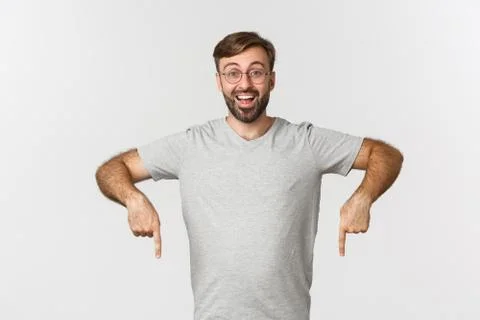 Cheerful bearded man smiling, pointing fingers down, showing logo, wearing gray Stock Photos