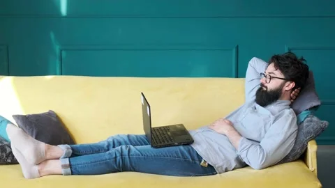 Cheerful bearded man using laptop, watching movie online, lying in bed. Stock Footage 153482068