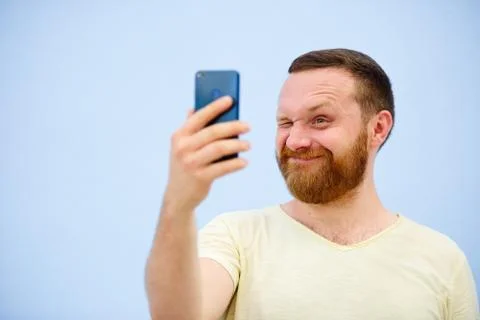 Cheerful bearded Man winks at the phone, suitable for advertising, on a blue  Stock Photos
