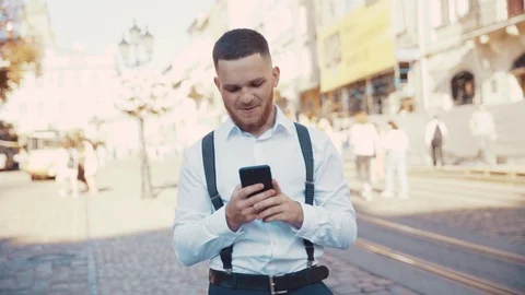 Cheerful bearded young man texting on smartphone in the crowded street at sunset Stock Footage 115666908