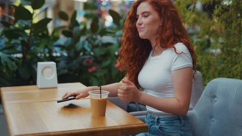 Cheerful beautiful young student girl sitting in a café, ends up a call, puts Stock Footage