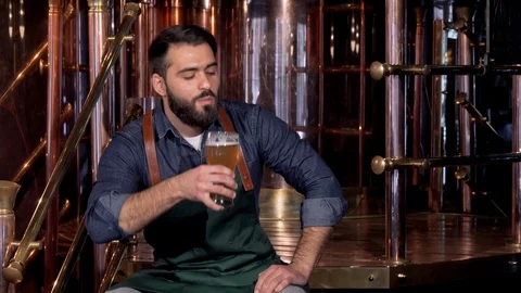 Cheerful beer maker resting at his brewery after working, drinking delicious Stock Footage 103049964