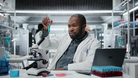 Cheerful biochemist in lab evaluates compound solutions for new drug formulation Stock Footage 325917956