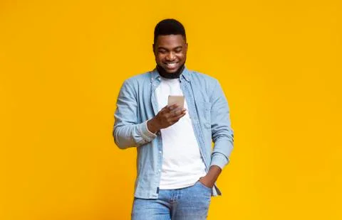 Cheerful black guy reading message on smartphone over yellow background Stock Photos