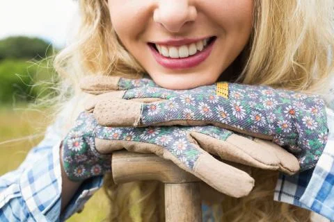 Cheerful blonde woman leaning on a shovel wearing gardening gloves Stock Photos