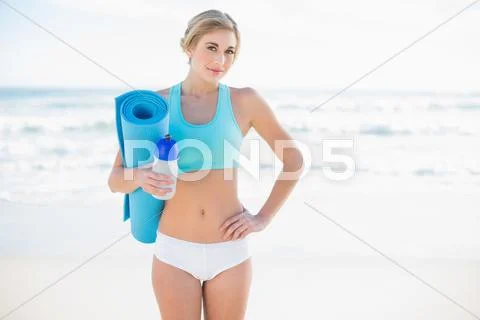Cheerful blonde woman in sportswear carrying a bottle and an exercise mat Stock Photos