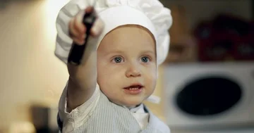 A cheerful boy in a culinary hat plays with a metal pan and pusher. Stock Footage 85803903