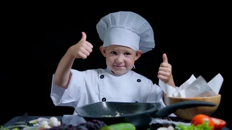 Cheerful boy is dancing and showing thumbs while cooking. He wears chefs suit Stock Footage 92556299
