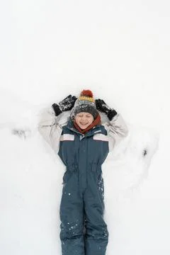 Cheerful boy lies in the snow and makes a snow angel. Happy childhood. Top vi Stock-Fotos