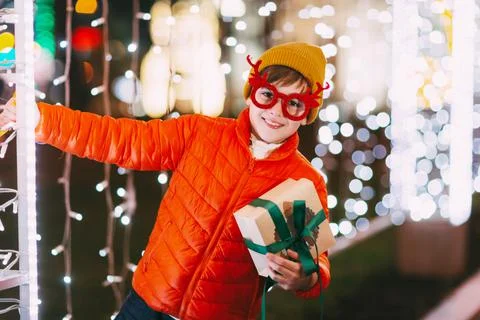 A cheerful boy in an orange jacket and funny glasses walks through the evening Stock Photos