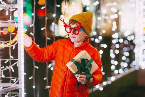 A cheerful boy in an orange jacket and funny glasses walks through the evening Stock Photos