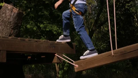 Cheerful boy passes an obstacle course on a rope road in the Park in the summer. Stock Footage 142079699