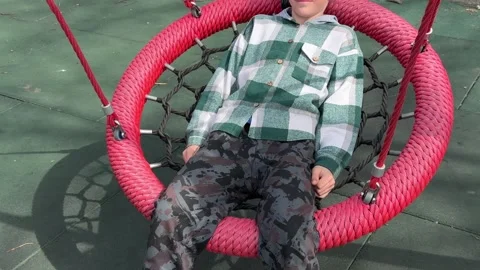 A cheerful boy plays on a round swing in the playground Video stock 335726550