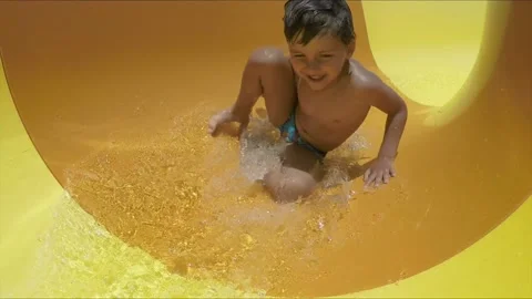 Cheerful boy is riding down rotating an orange slide in a water park Stock-Footage 130254284
