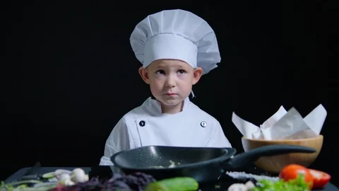 Cheerful boy shows thumb while cooking. He wears chefs suit and cap. Black Stock Footage 92555965