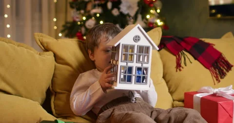 Cheerful boy sits on sofa and enjoys game with Christmas house Video stock 316749250