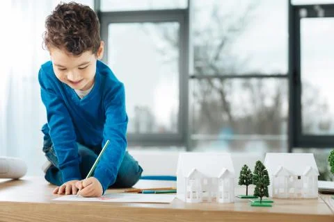Cheerful boy sitting on the table and drawing Stock Photos