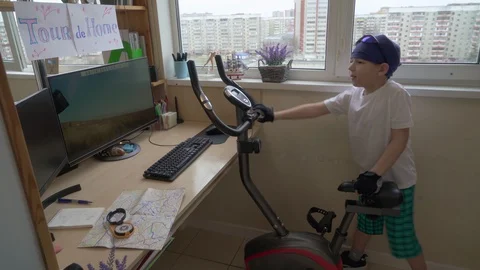 Cheerful Boy Is Training On Exercise Bike At Home. Indoor Cycling 動画素材 129586930