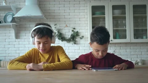 Cheerful boys actively move listening to music, sit at the table. One kid plays Stock Footage