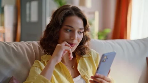 Cheerful brunette browsing mobile phone in light apartment living room closeup. Stock Footage 333316185