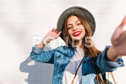 Cheerful brunette girl in white wristwatch and gray hat posing in front of Stock Photos