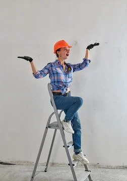 A cheerful builder in a helmet sits on a stepladder Stock Photos