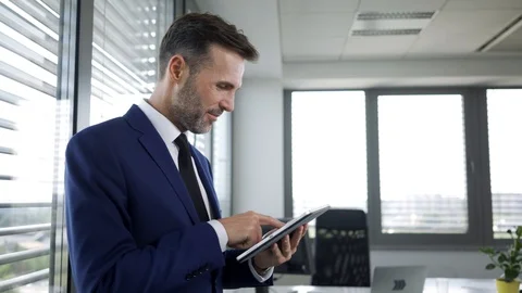 Cheerful businessman using tablet and leaning against office windows Stock Footage 114813069