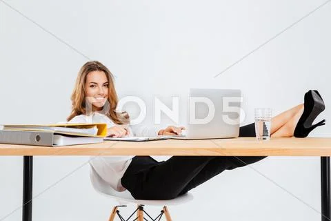 Cheerful businesswoman sitting and using laptop with legs on table Stock Photos