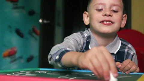 Cheerful Caucasian boy solves a mathematical problem, writes in chalk on a black Stock Footage 134420564